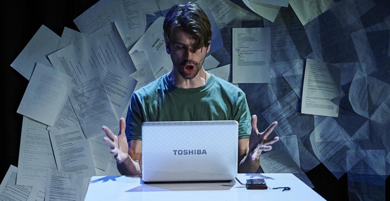 A man is on stage sitting in front of a computer