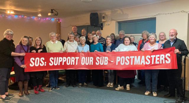 Rockspring Community Choir holding SOS Support our Sub-postmasters red banner