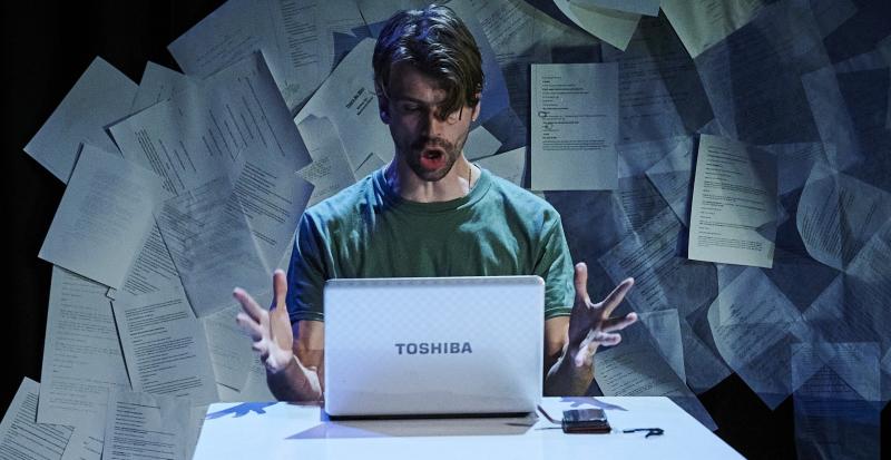 A man is on stage sitting in front of a computer